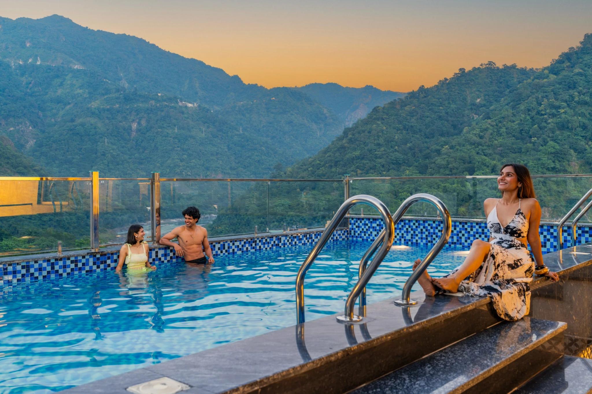 Three guests relaxing at the rooftop pool at golden hour, mountains behind